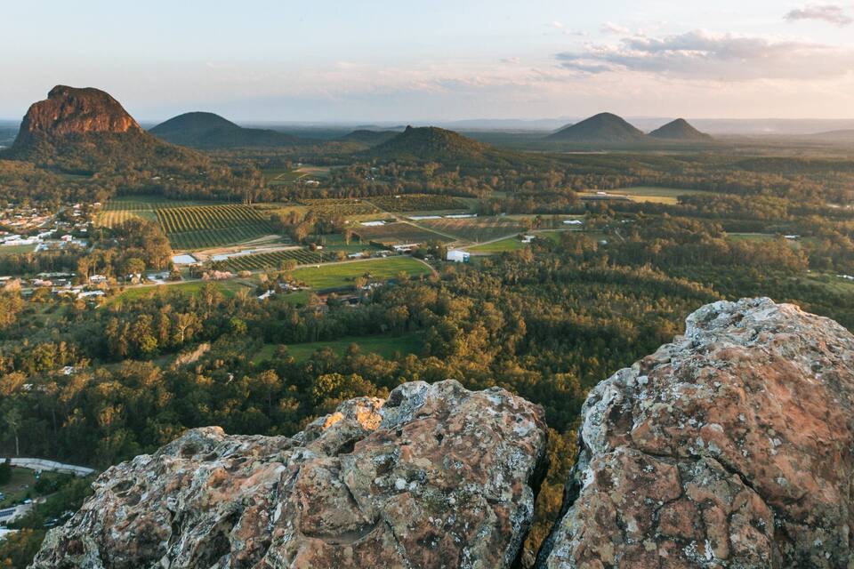 A mountainous landscape with a prominent rocky outcrop in the foreground, a valley with agricultural fields, and distant hills.