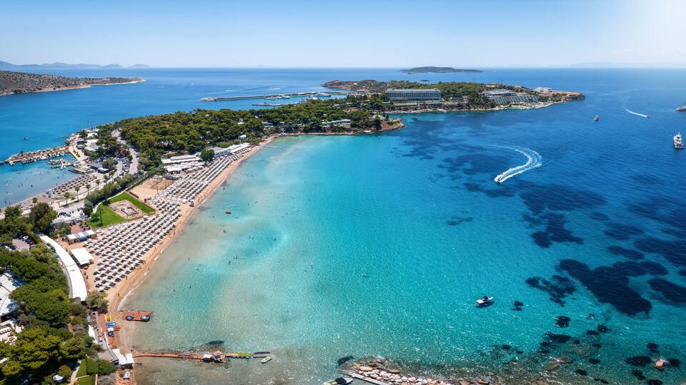 A coastal town with a clear blue sea, a sandy beach, and a small island with buildings.