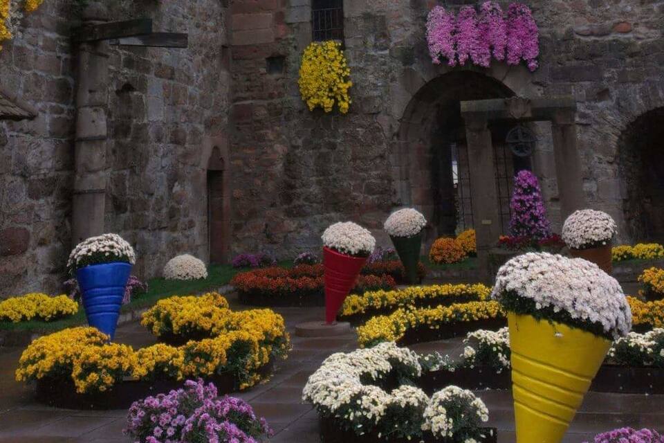 A historic stone building with a conical roof, adorned with colorful flower arrangements.
