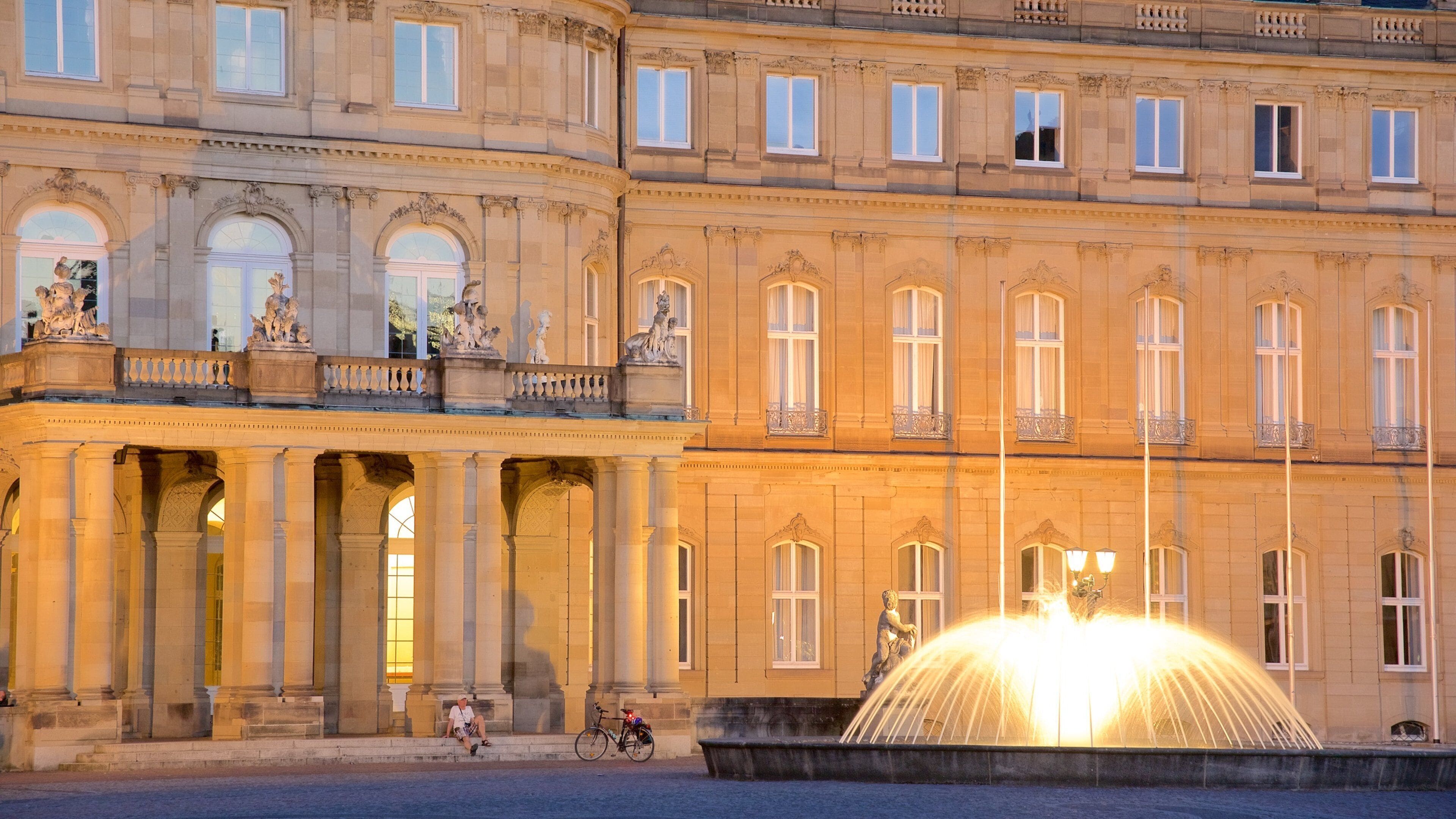 A historic building with classical architecture, including columns and statues, and a fountain in the foreground.