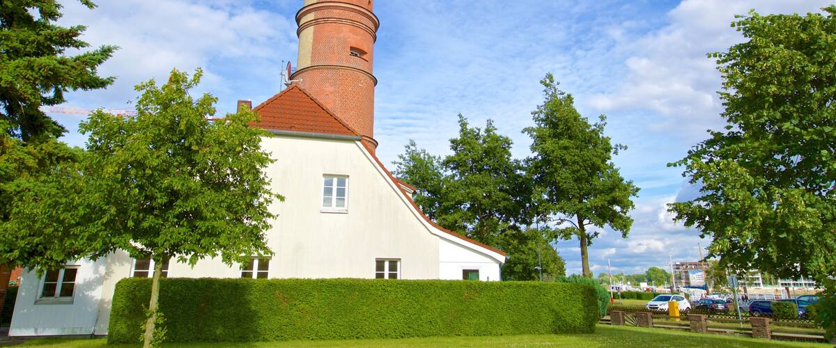 A church with a tall brick tower and white walls, surrounded by trees and a well-maintained hedge.