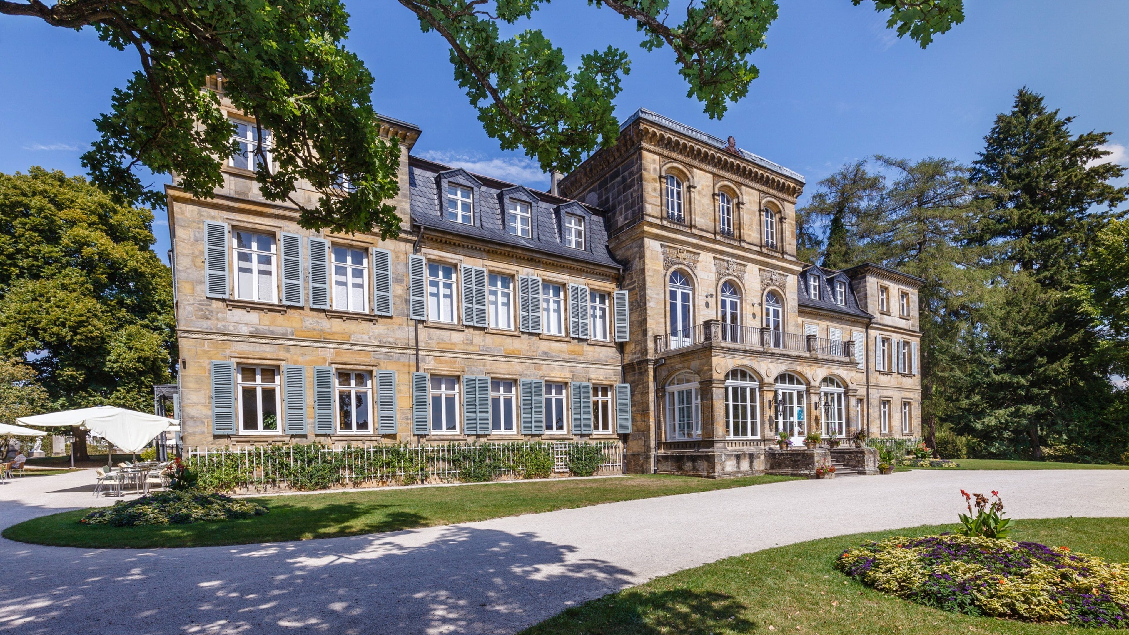 A large, historic building with multiple windows and a well-maintained garden.