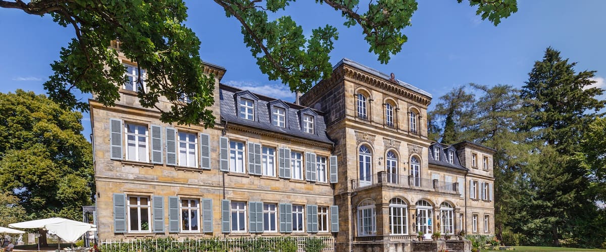 A large, historic building with multiple windows and a well-maintained garden.