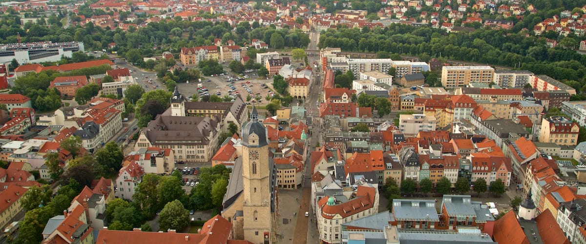 A panoramic view of a historic town with a prominent church tower, dense residential areas, and rolling hills in the background.