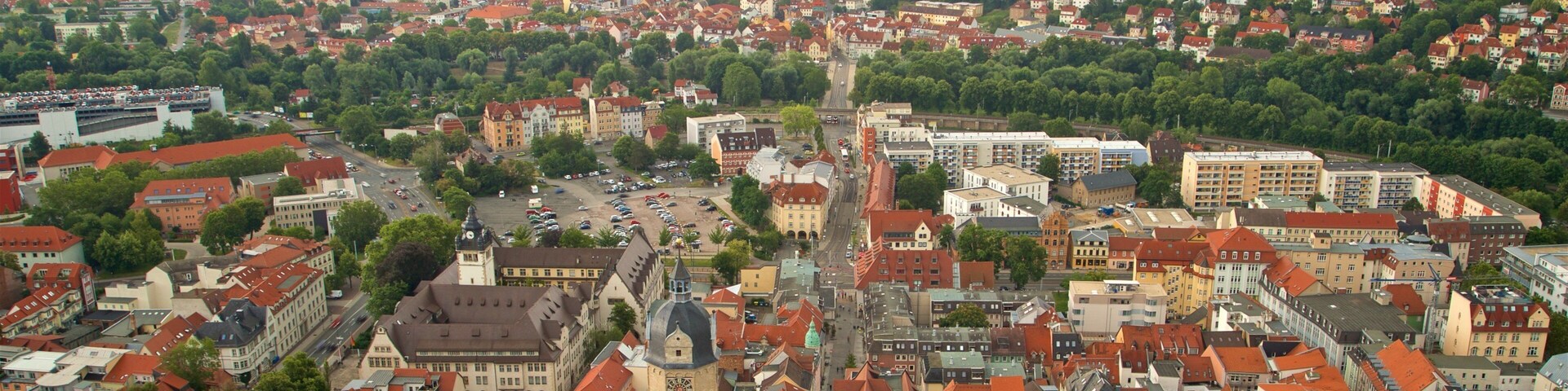 A panoramic view of a historic town with a prominent church tower, dense residential areas, and rolling hills in the background.