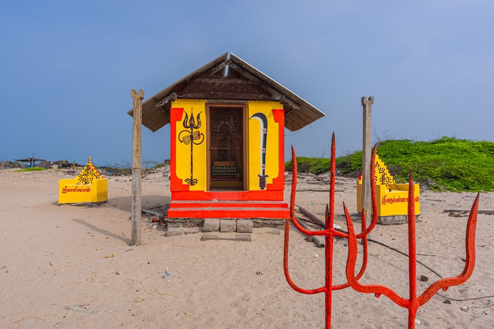 Una pequeña cabaña colorida con techo triangular y una puerta, rodeada de estructuras rojas similares a tridentes y cajas amarillas con texto.