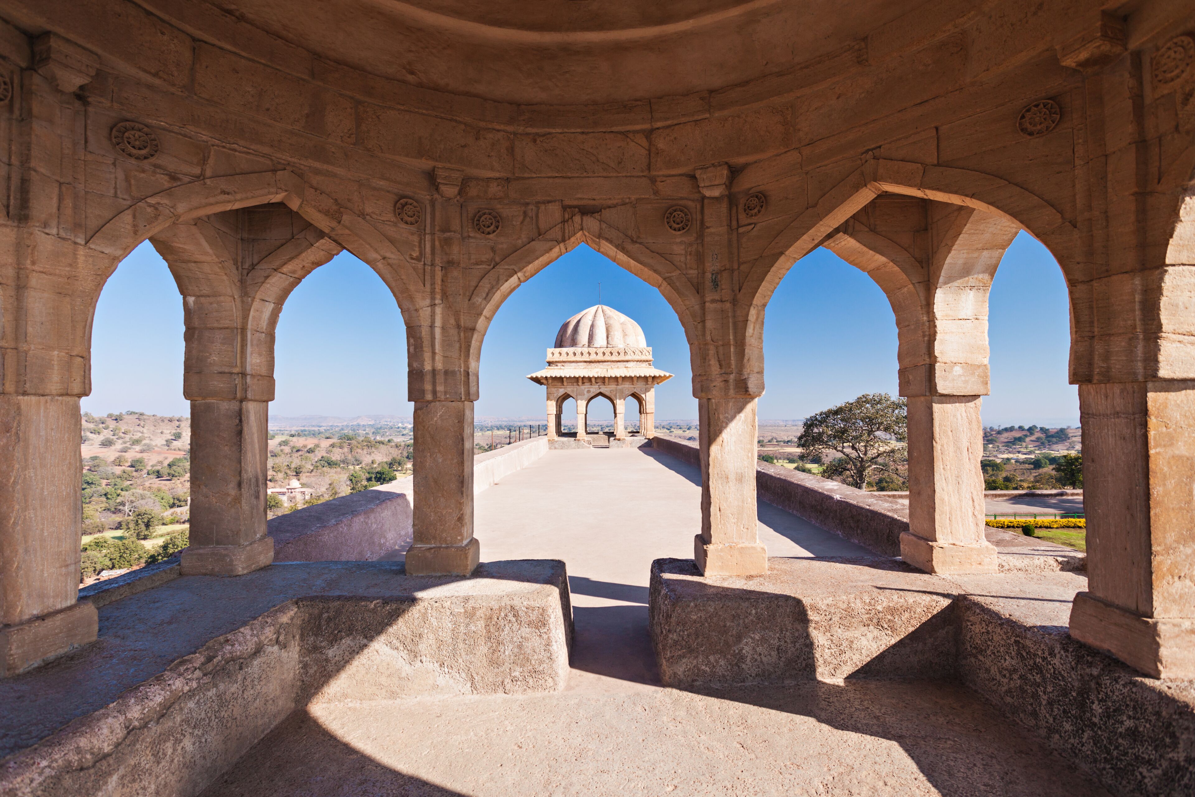 A stone archway with a dome structure in the distance.