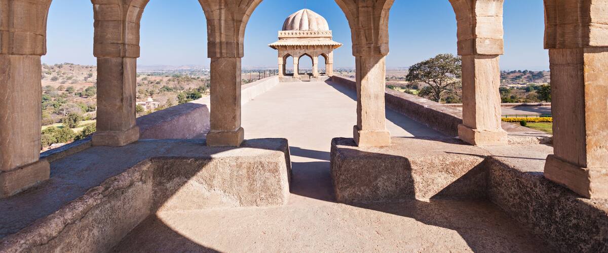 A stone archway with a dome structure in the distance.