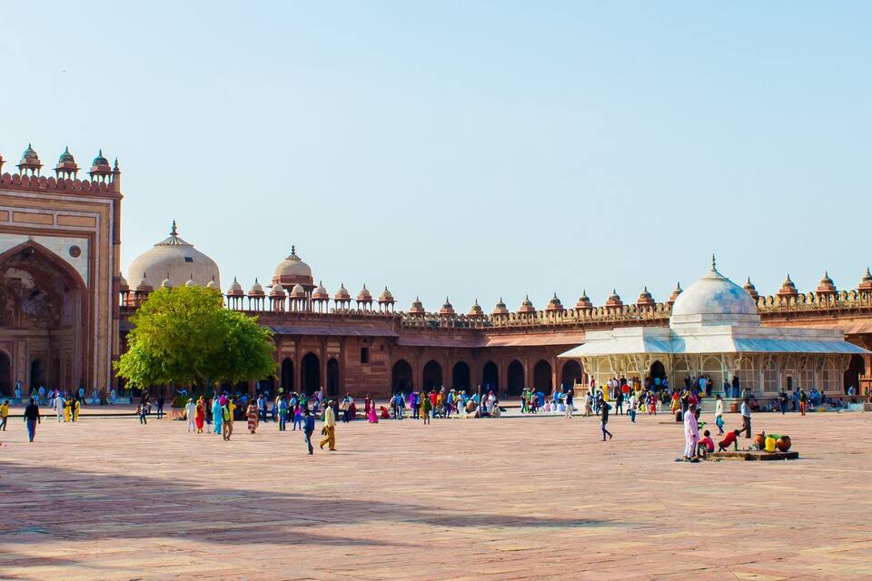A large open courtyard with a historic building featuring domes and arches.