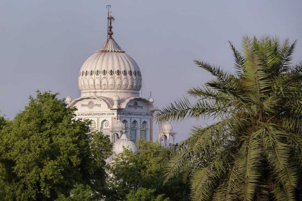 Un edificio blanco de cúpula con diseños intrincados y una aguja, rodeado de frondosos árboles verdes.