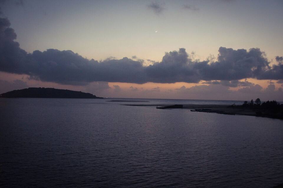 Une mer calme au crépuscule, avec un croissant de lune et des nuages.