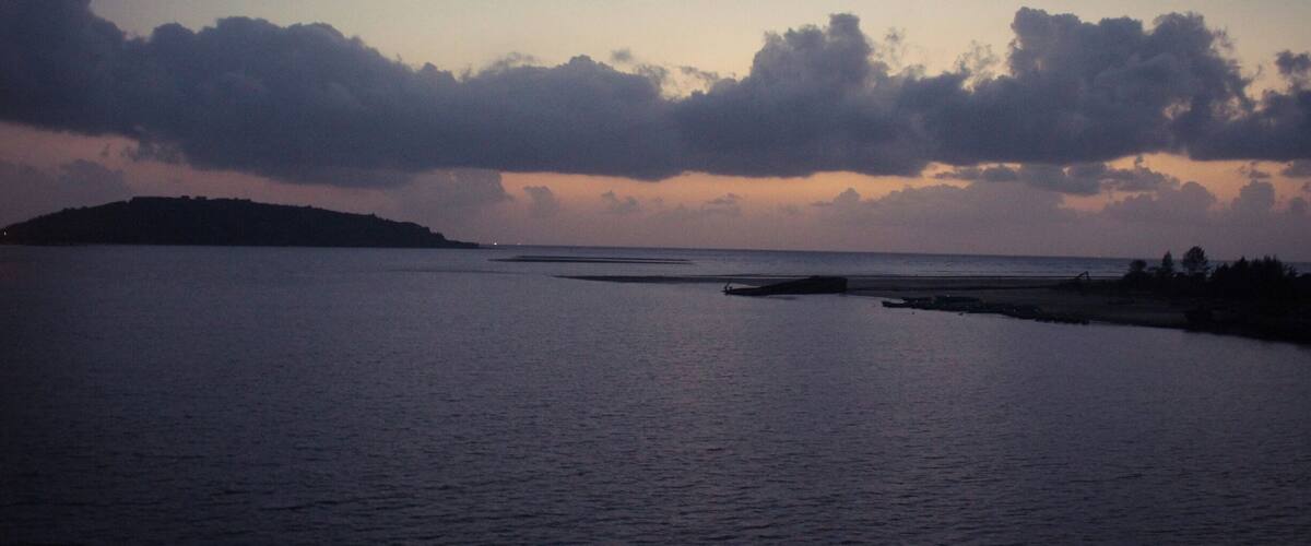 A calm sea at dusk with a crescent moon and clouds.