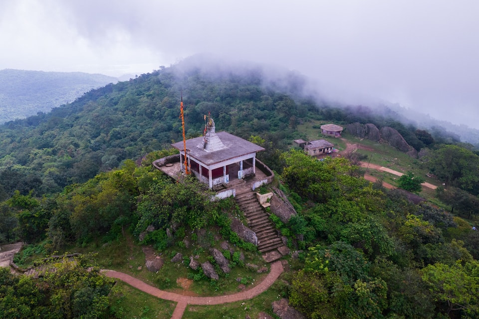 A temple on a hilltop surrounded by lush greenery and misty mountains.