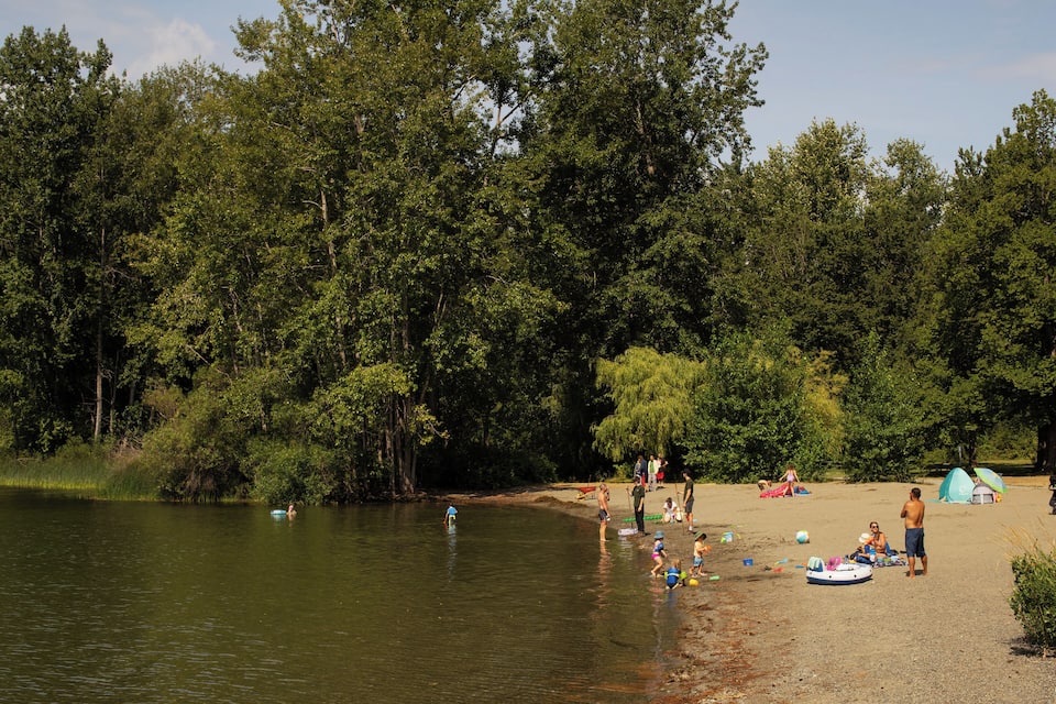 Un camping junto al lago con tiendas de campaña, personas y botes.