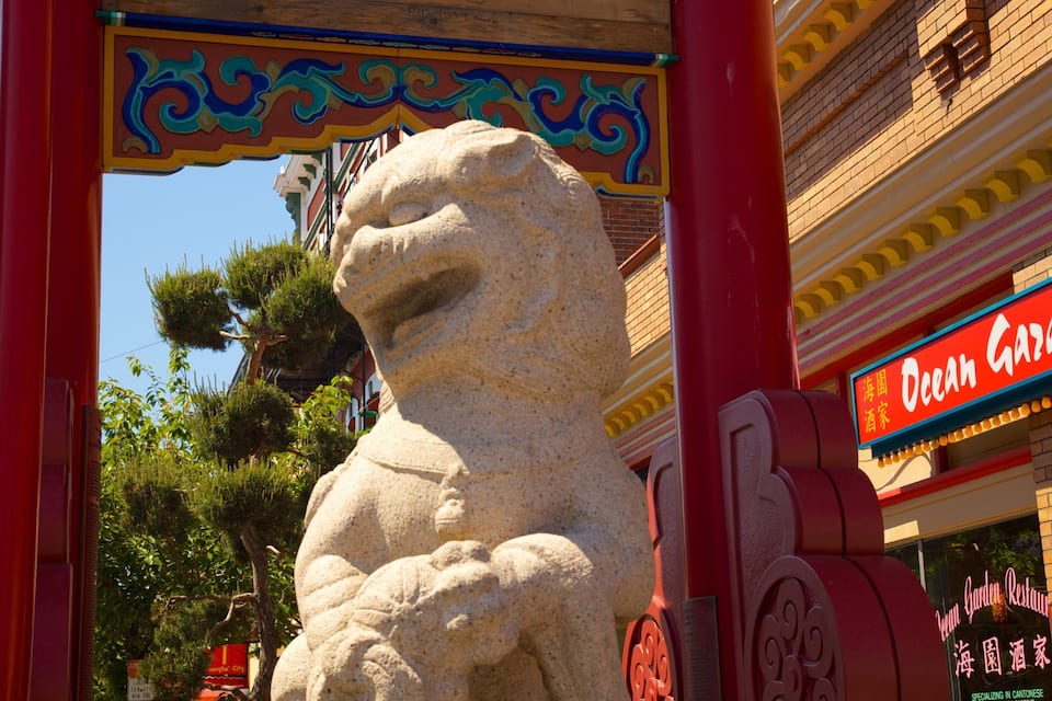 Una estàtua de lleó de pedra sota un arc decoratiu, amb un rètol de restaurant al fons.