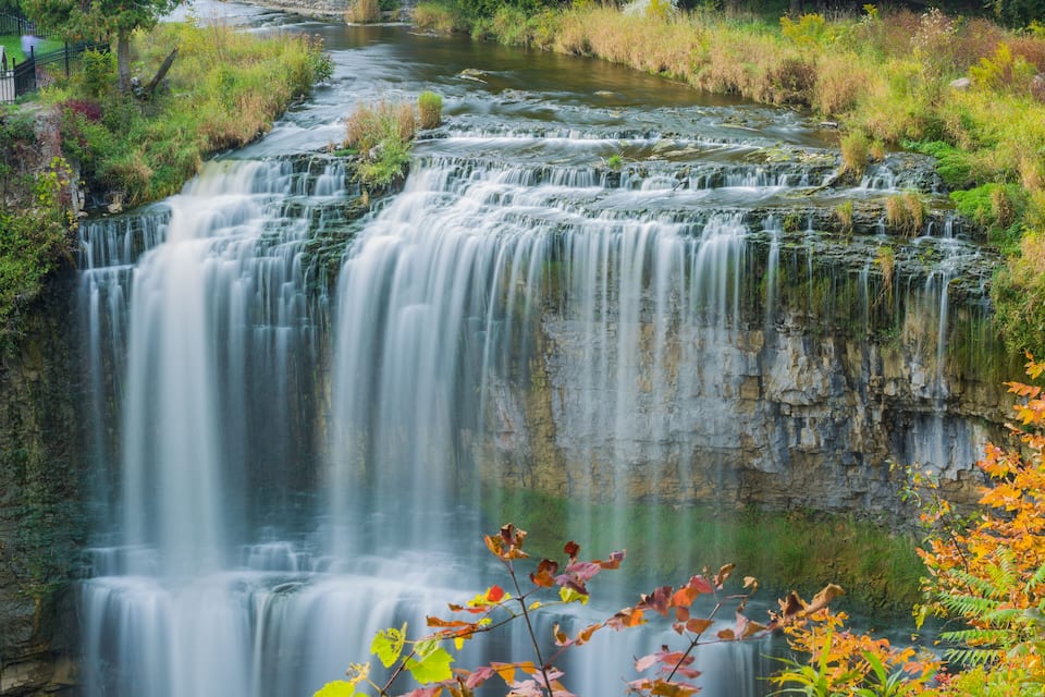 A multi-tiered waterfall with surrounding greenery and a river.