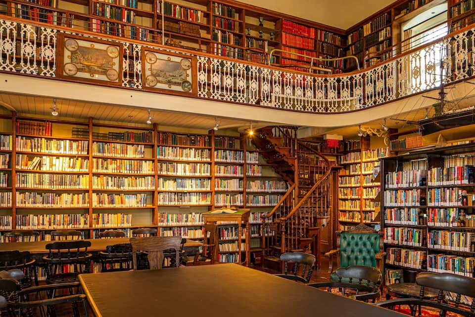 Eine imposante Bibliothek mit mehreren Regalböden, einer Wendeltreppe und einem großen Lesetisch.