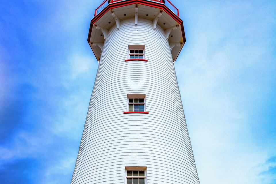 Ein hoher, weißer Leuchtturm mit roten Akzenten und drei Fenstern.