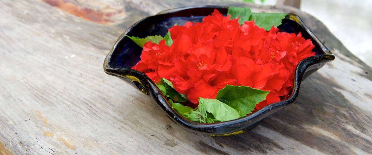 A black ceramic bowl filled with red flowers on a wooden surface.