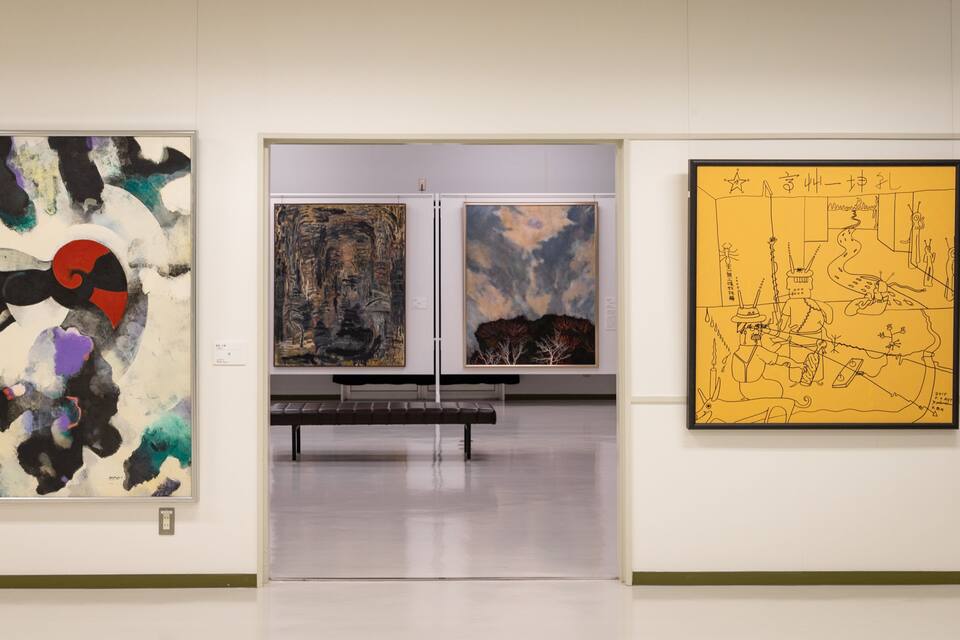 Una galería de arte con pinturas abstractas y un gran mural amarillo.