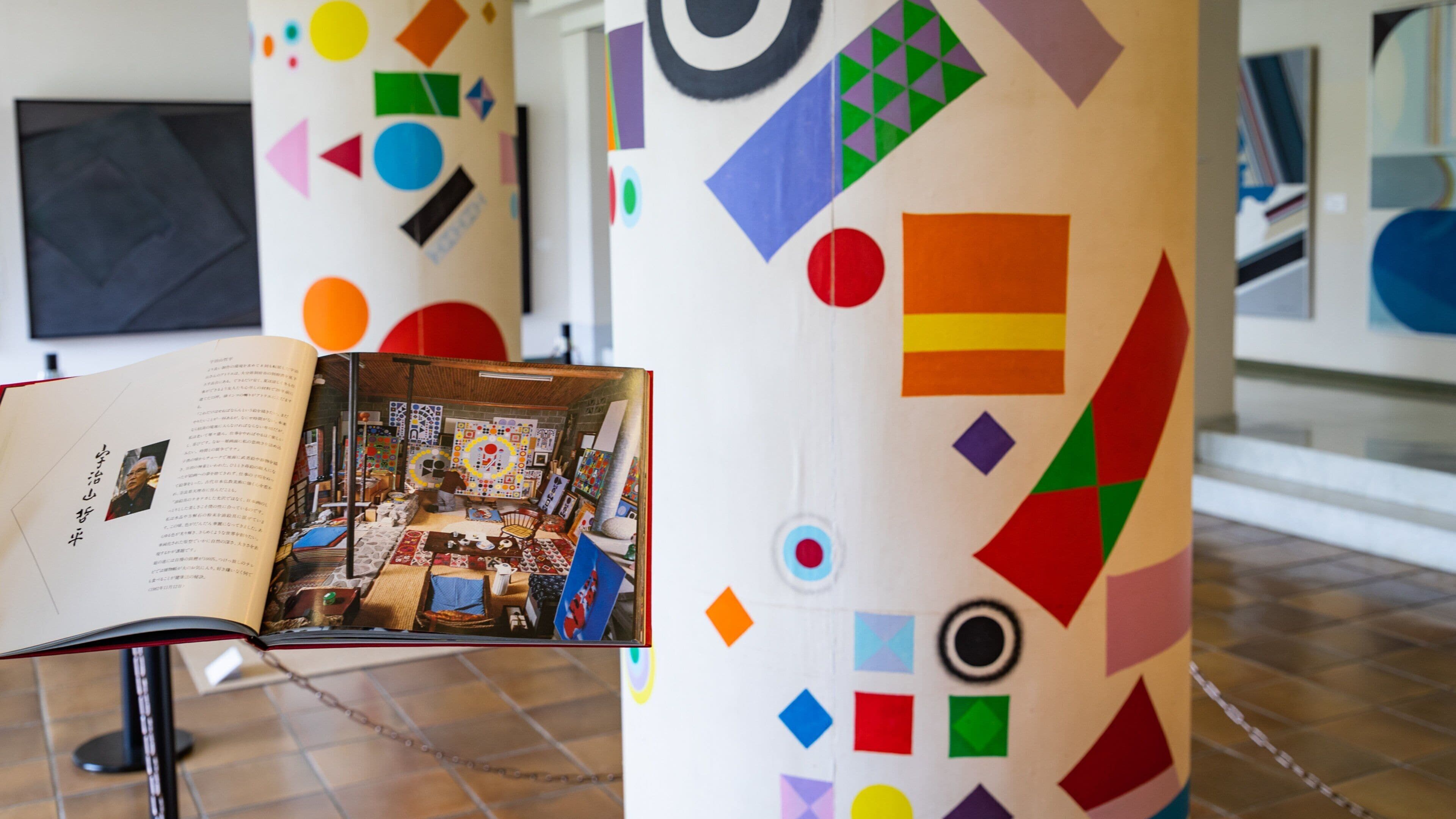 An art gallery with colorful geometric patterns on the walls and a book open on a stand.