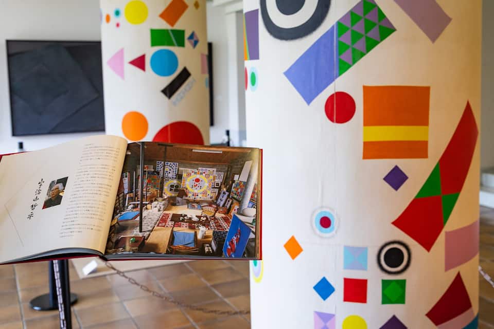 An art gallery with colorful geometric patterns on the walls and a book open on a stand.