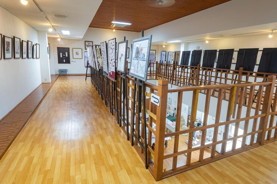 Una galería de arte con pisos de madera y un largo pasillo que exhibe obras enmarcadas.