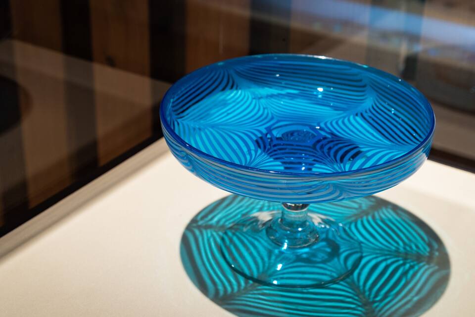 Un cuenco de vidrio azul con un diseño texturizado, expuesto sobre un pedestal.