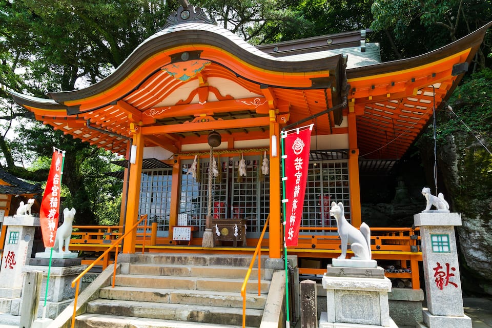 Un santuario japonés tradicional con techo curvo, estatuas de piedra y banderines rojos.