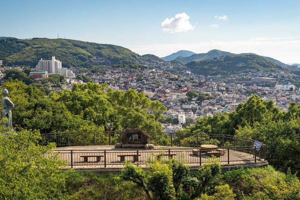 Un parque con una estatua, un monumento de piedra y un paisaje urbano al fondo.