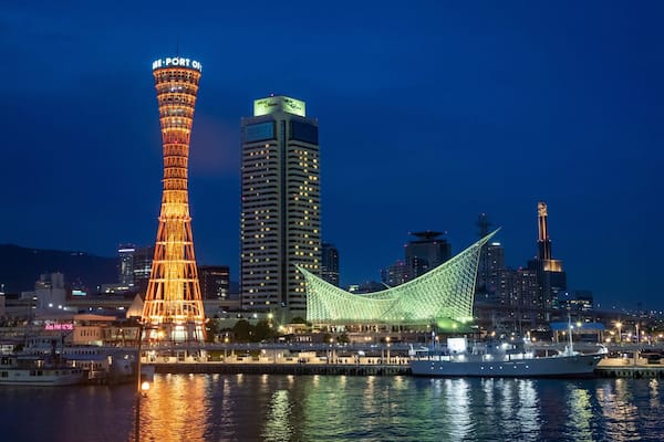 Nachtansicht einer Stadt mit beleuchteten Gebäuden, einem markanten Turm und einer grün beleuchteten Brücke.