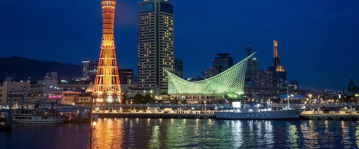 A city skyline at night with illuminated buildings, a prominent tower, and a green-lit bridge.