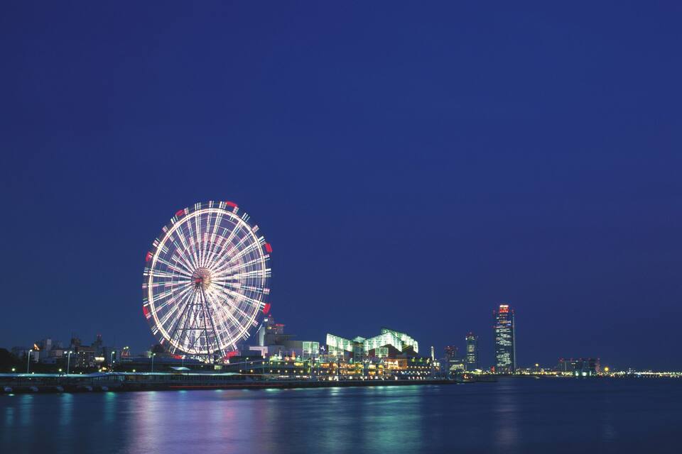 Una grande ruota panoramica di notte con le luci della città riflesse sull'acqua.