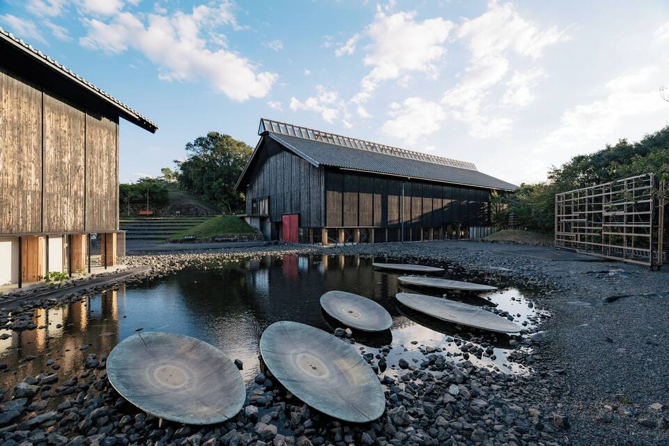 A wooden building with a metal roof, a pond with stepping stones, and a gravel path.