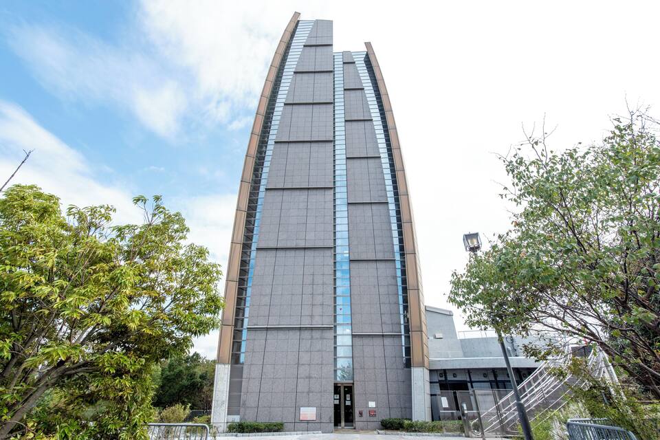 A tall, modern building with a symmetrical design, surrounded by trees and a clear sky.