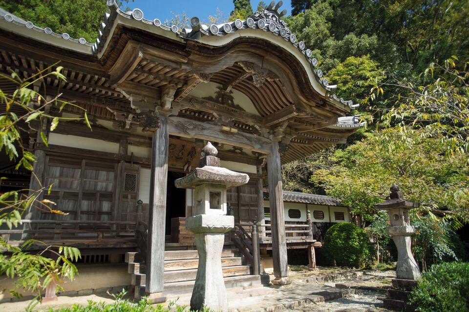 Um templo japonês tradicional com arquitetura ricamente decorada, lanternas de pedra e um jardim tranquilo.