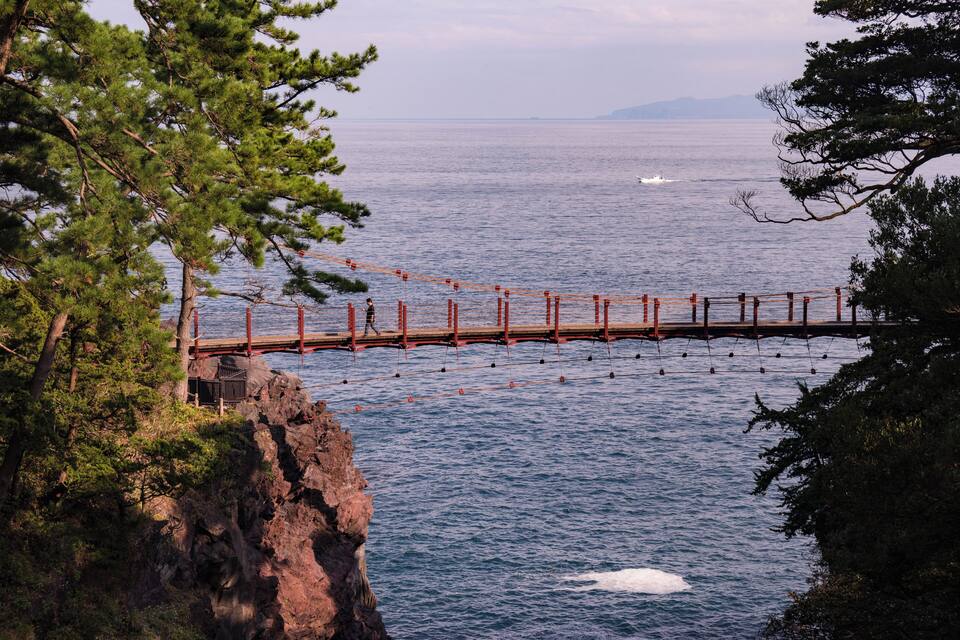 A wooden bridge over a body of water, surrounded by trees and rocky terrain.