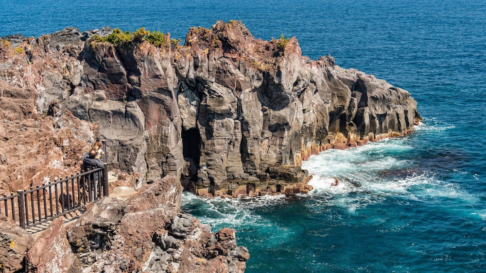 A rocky coastline with a railing and waves crashing against the rocks.