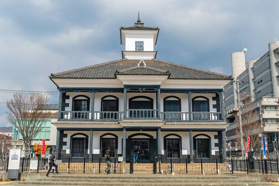 A historic building with a tiled roof, a central tower, and a balcony with black railings.