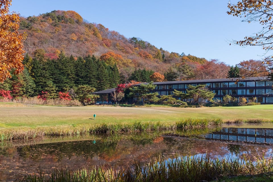 A golf course with a pond, autumn-colored trees, and a building in the background.