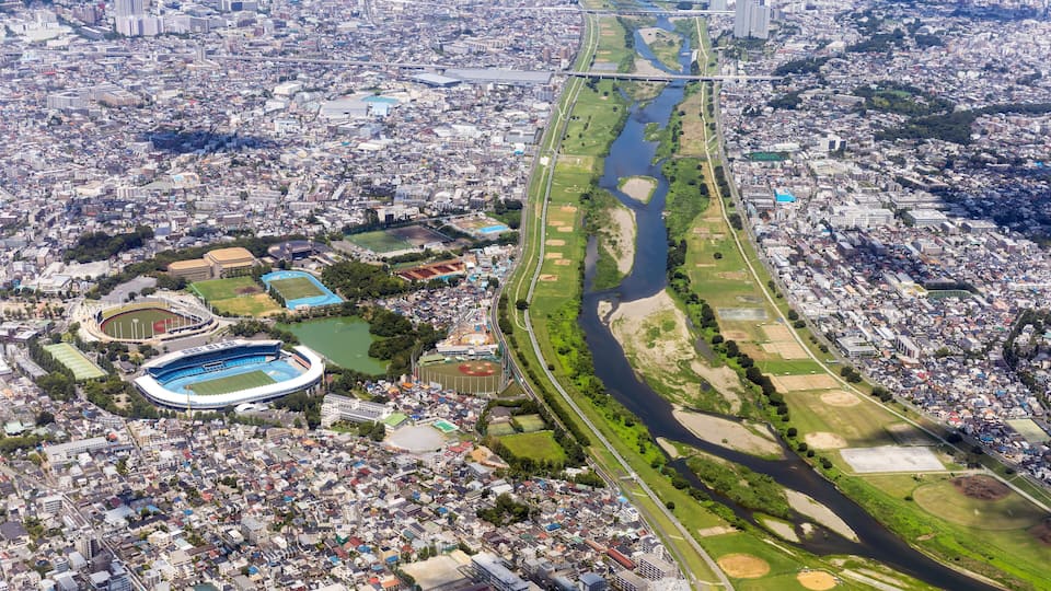 An aerial view of a city with a river running through it, surrounded by green spaces and a stadium.