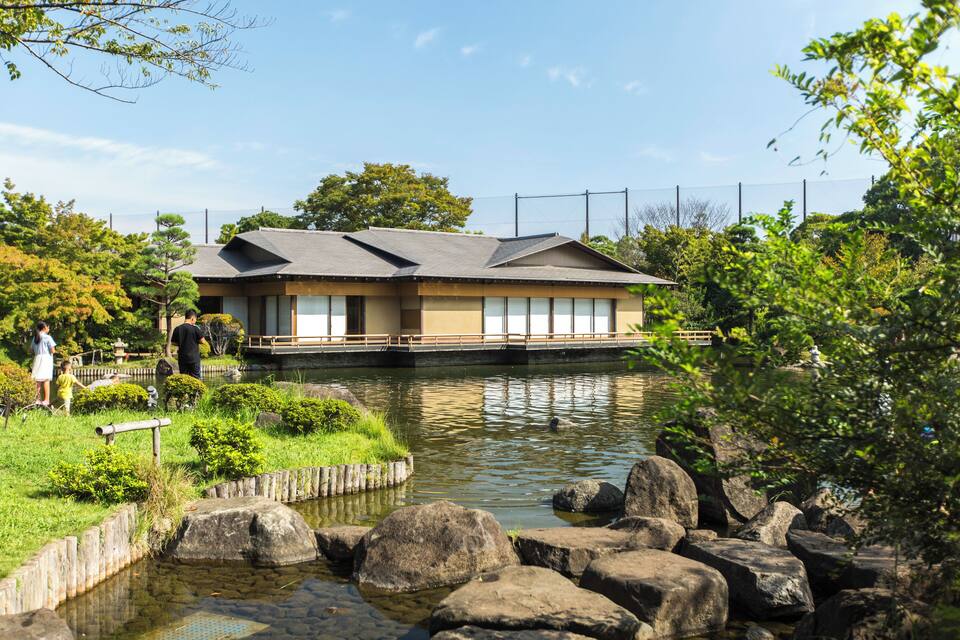 Un edificio japonés tradicional junto a un estanque tranquilo con rocas y vegetación.