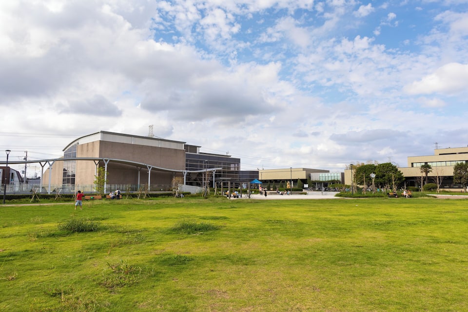 A modern building complex with a large grassy field in front.