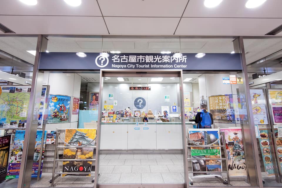 Der Eingang zum Informationszentrum für Touristen in Nagoya mit Informationsplakaten und einer digitalen Uhr.