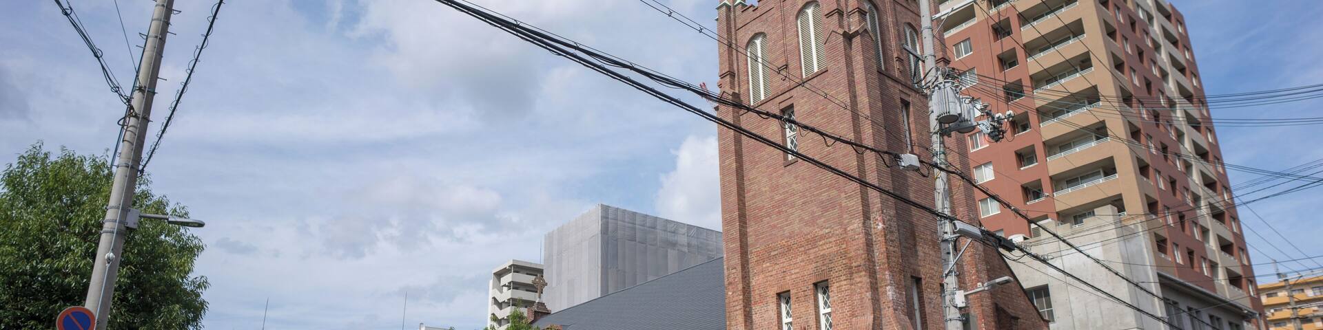 A red brick church with a tower, a modern building, and a street with a crosswalk.