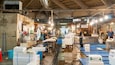 Een levendige vismarkt, met medewerkers die vis verhandelen, tafels met dozen vis en borden in een vreemde taal.