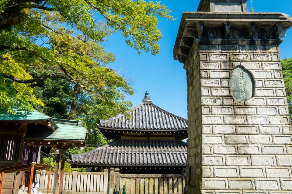A traditional Japanese building with a tiled roof and a stone pillar with inscriptions.