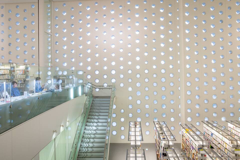 Een modern bibliotheekinterieur met een opvallend plafondontwerp, inclusief ronde uitsparingen, glazen balustrades en boekenplanken.