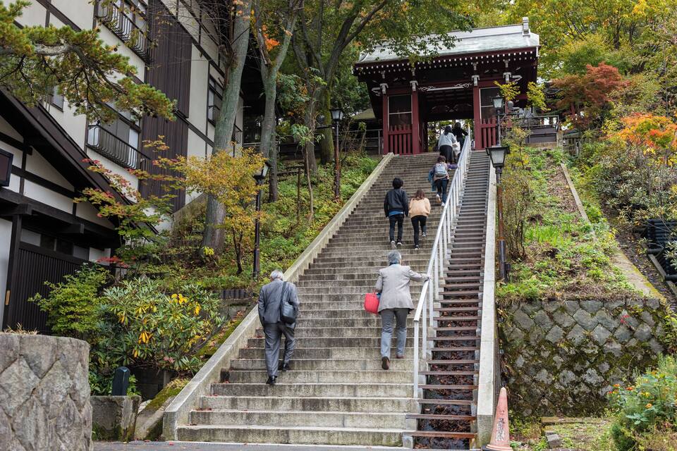 Degraus de pedra levam a uma construção japonesa tradicional, cercada por árvores e folhagem.