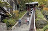 Un escalier en pierre menant à une construction traditionnelle japonaise, entourée d’arbres et de feuillage.